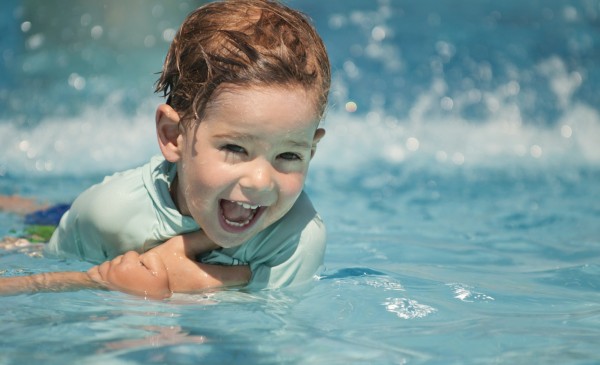 Cute boy desparately holding for parents hand in a swimming class. Selective focus, polarizing filter