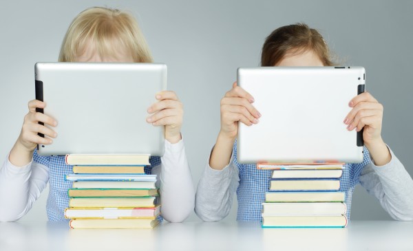 Two pupils leaning on a pile of books while reading on touchpad