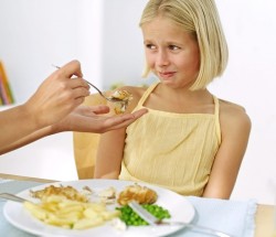 Mother's Hand Feeding Food to a Young Girl (13-14) Who Is Making a Face