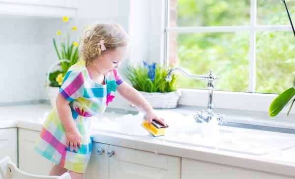 Cute toddler girl in colorful dress cleaning table on kitchen