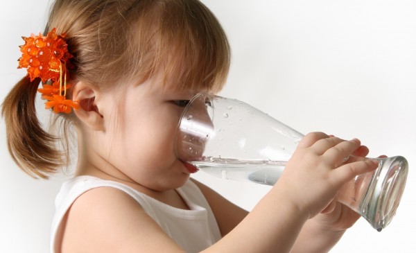 The small girl is drincking water from glas.